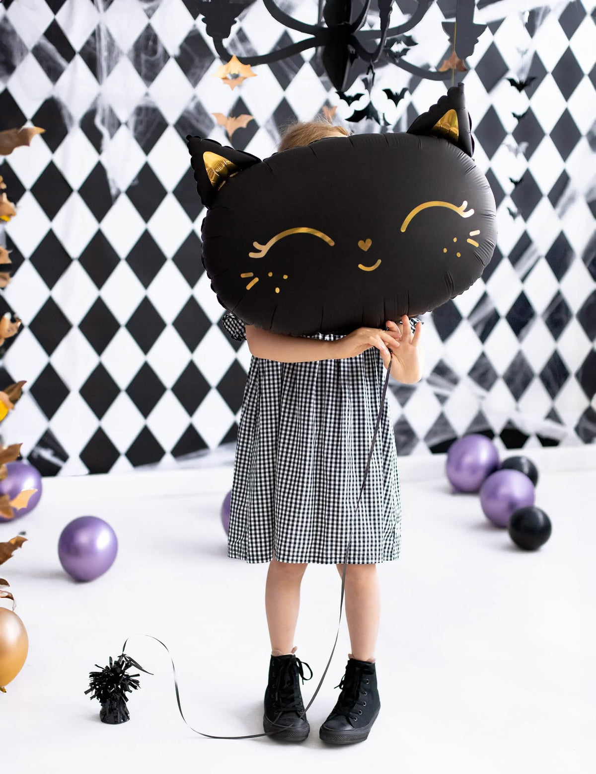 copil ținând în fața feței sale balonul din aluminiu pisici pentru halloween