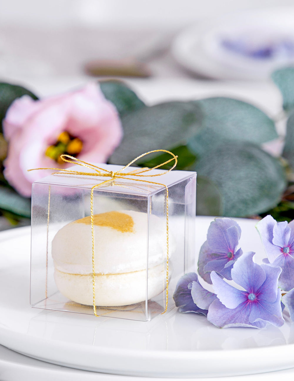 Gros plan sur le macaron et le ruban doré des petites boîtes pour cadeaux pour invités transparentes