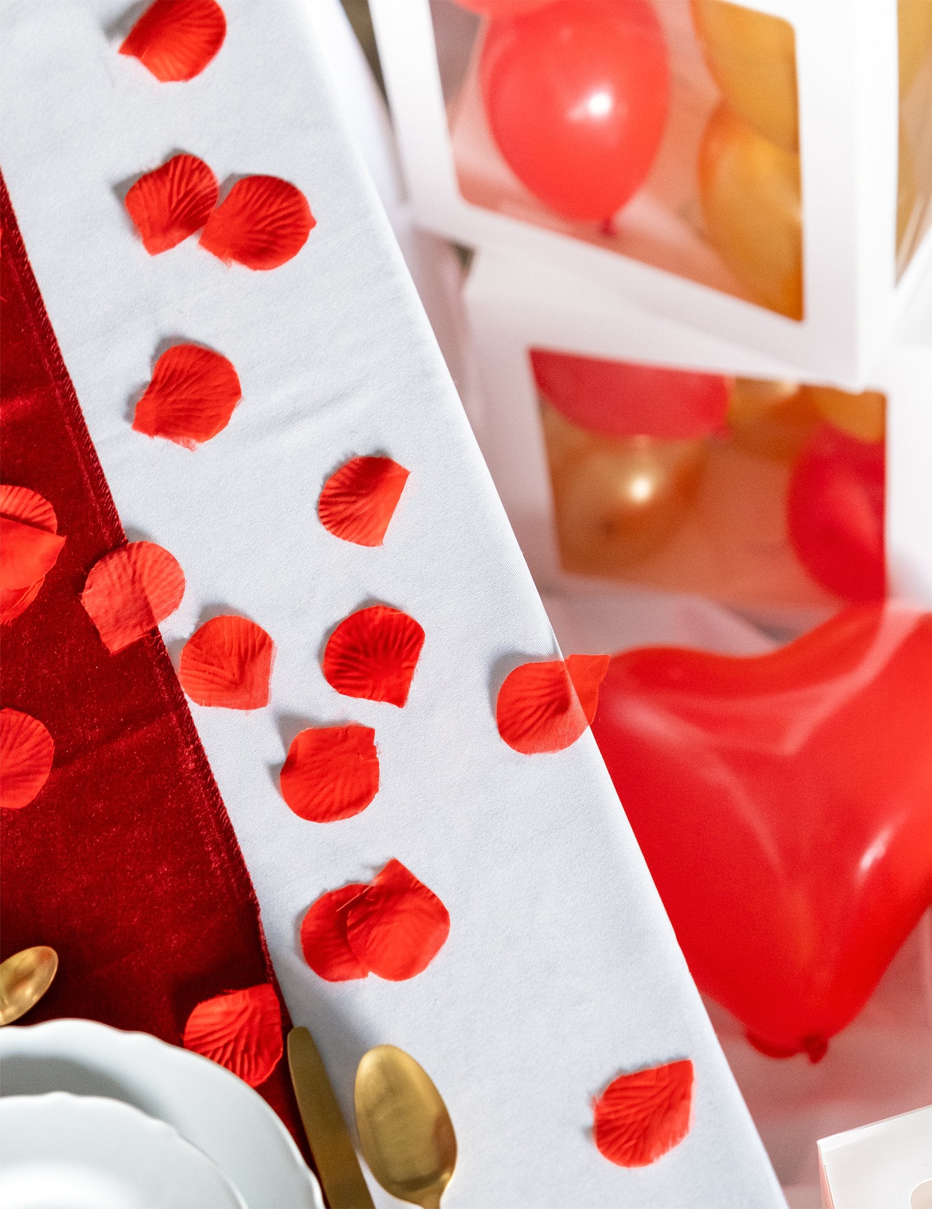 Mise en situation sur une table des pétales de rose pour décoration en tissu rouge