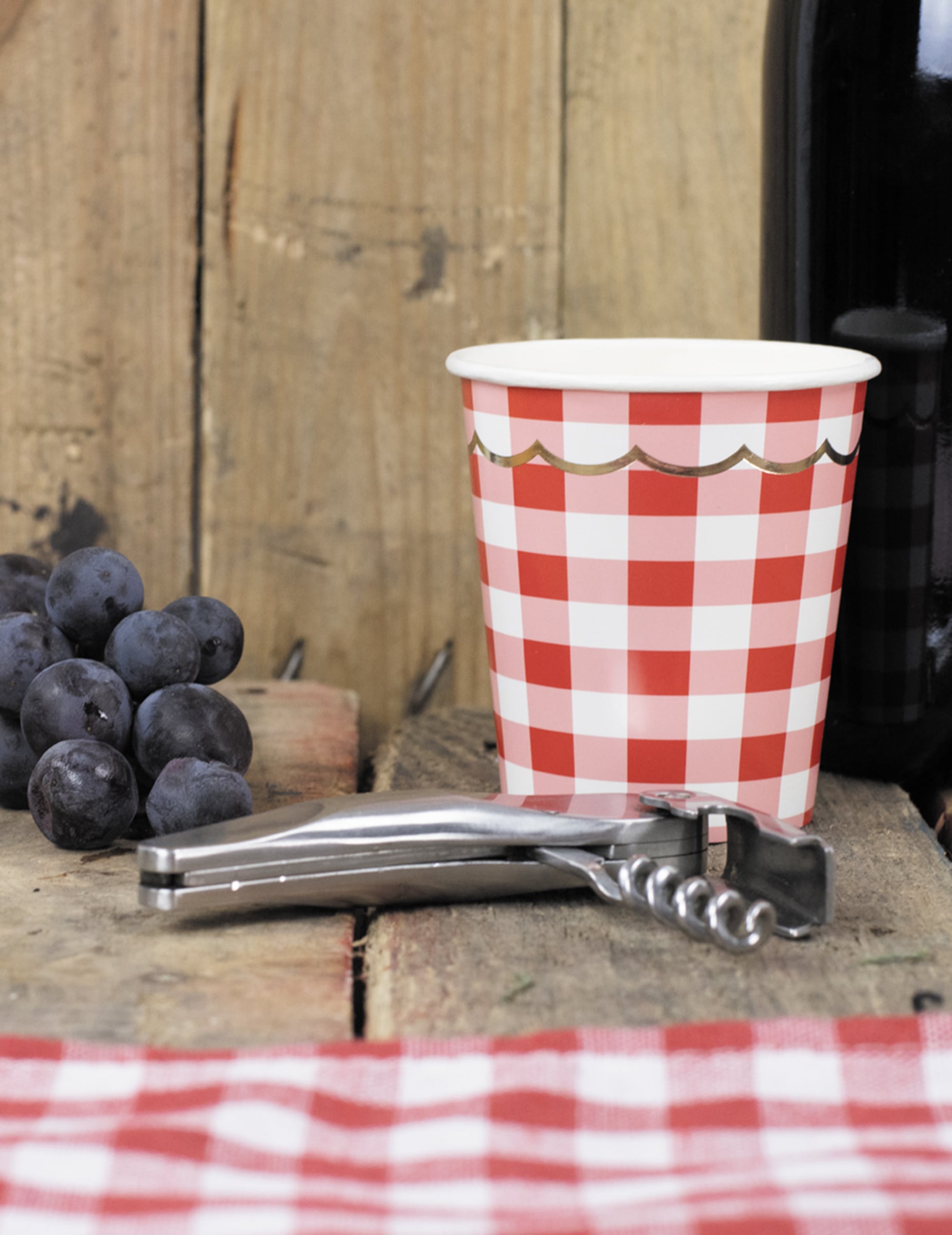 Mise en scène avec tire-bouchon et raisins du gobelet en carton festonné vichy pour fête rouge et blanc