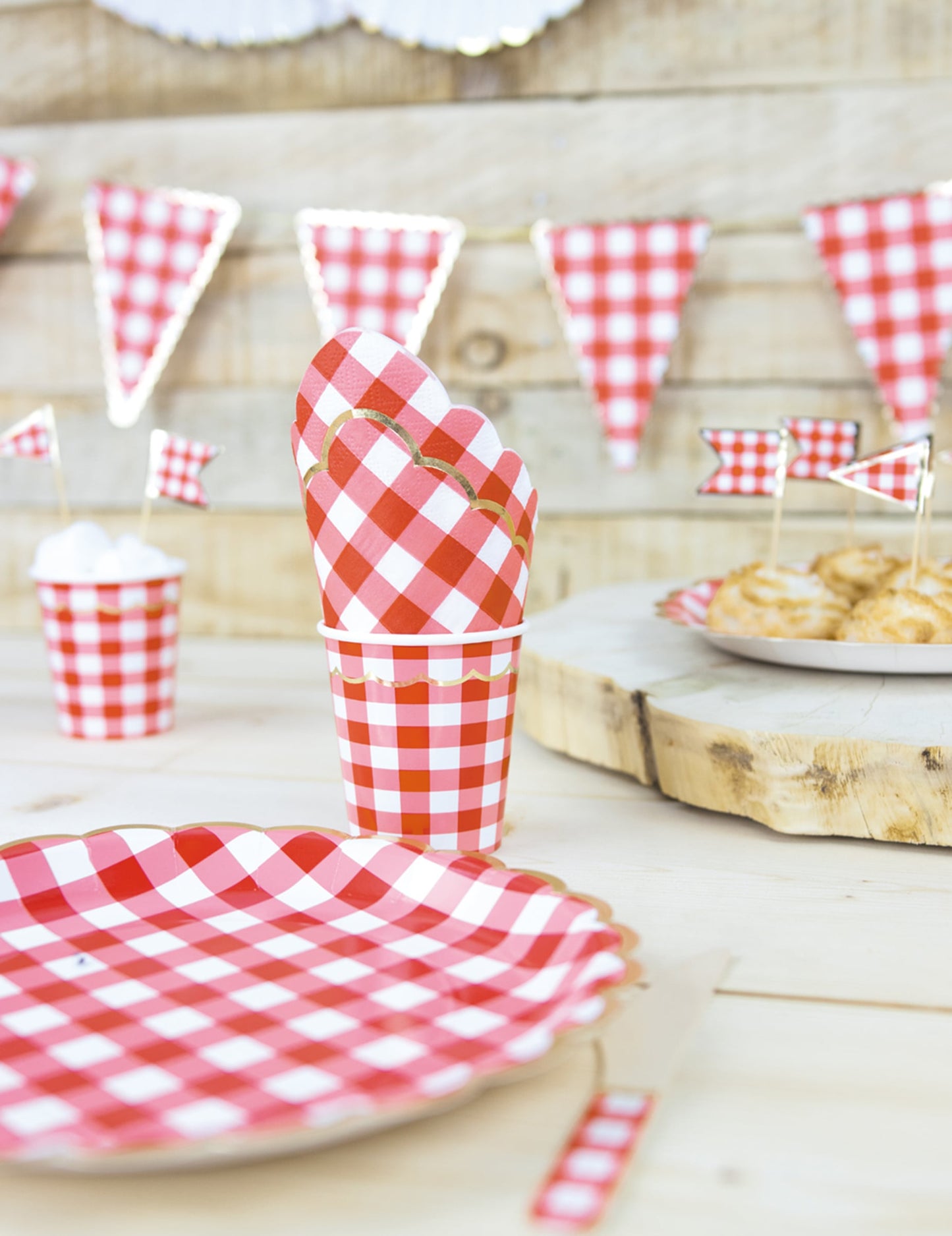 Mise en scène avec assiette et fanions du gobelet en carton festonné vichy pour fête rouge et blanc