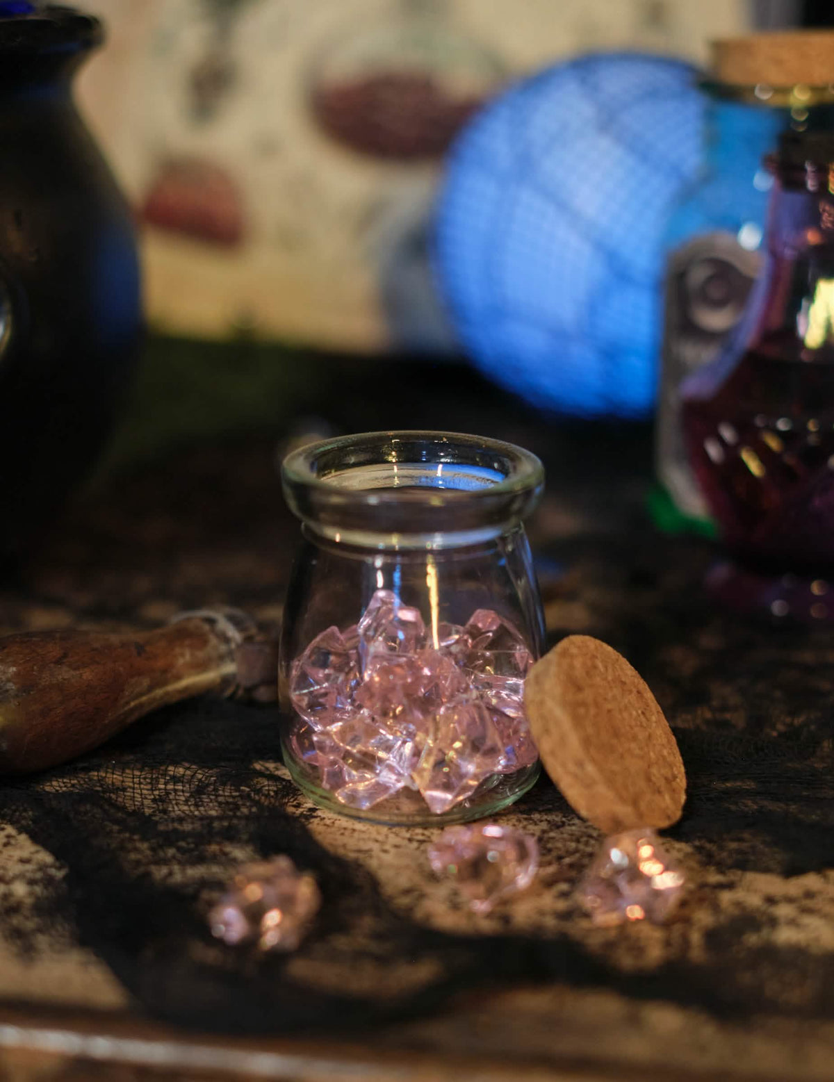 Detaliu al cristalelor împrăștiate în fața borcanului cu pietre cu efect de cristal pentru decorațiuni de masă roz